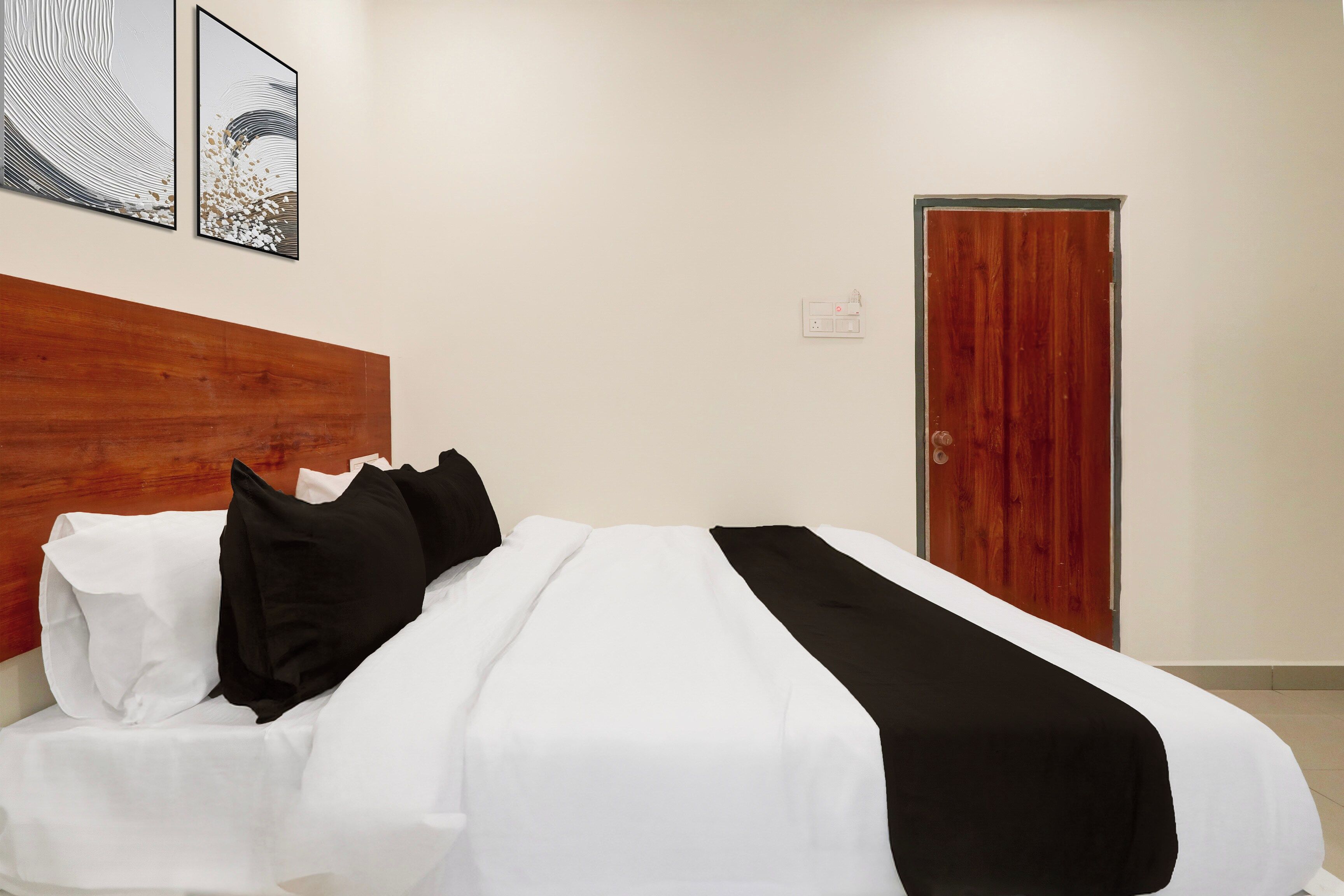 Una habitación de hotel con cabecera de madera, cama con ropa de cama blanca y negra, y dos obras de arte enmarcadas en la pared.