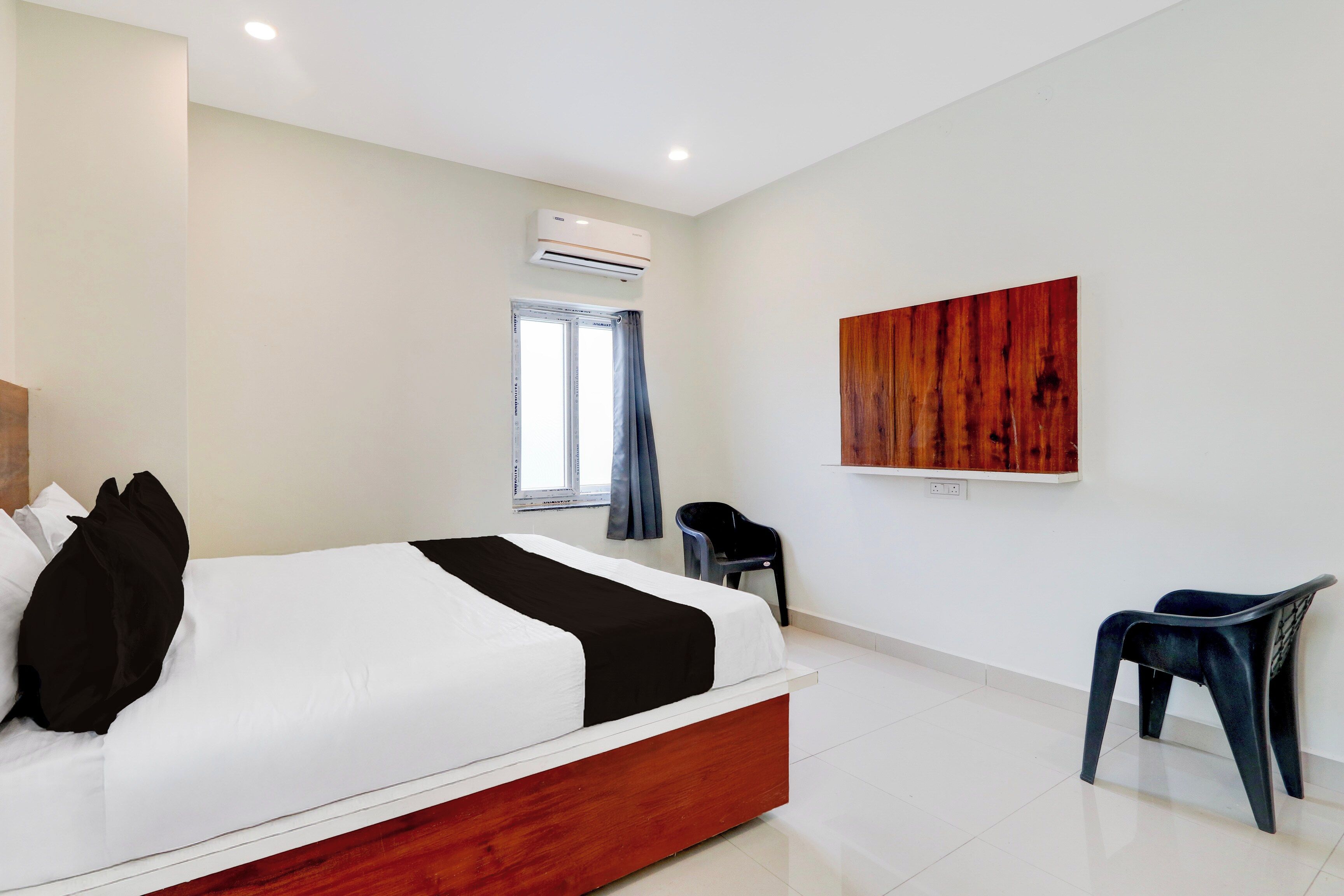 Una habitación de hotel con cama, una silla, un ventanal con cortinas, un equipo de aire acondicionado y una obra de arte colgada en la pared.