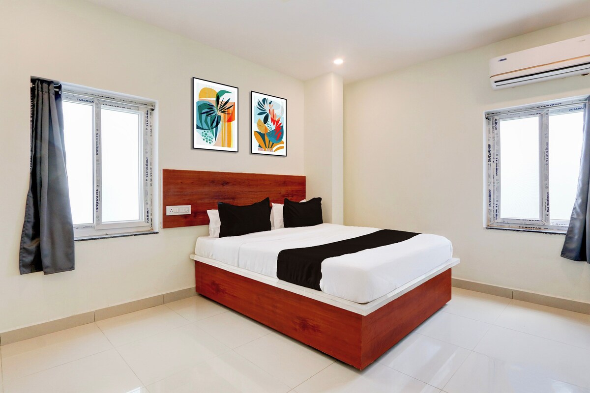 A bedroom with a wooden headboard, a bed with white and black bedding, two abstract paintings on the wall, and an air conditioning unit on the wall.