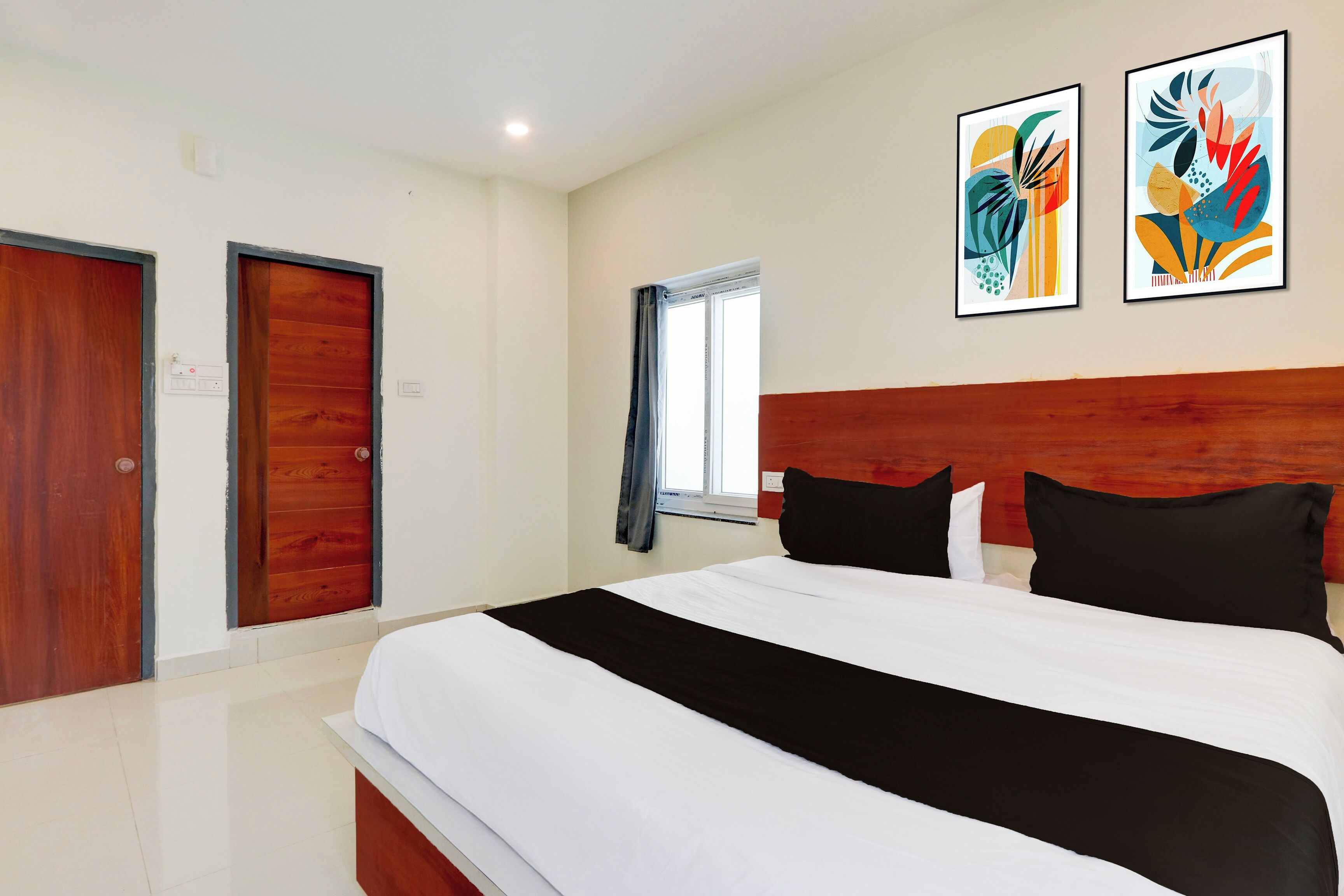 Habitación de hotel con una cama grande, dos puertas, una ventana con cortinas y dos obras de arte colgadas en la pared.