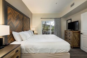 Ein Hotelzimmer mit einem großen Bett, einem Fernseher, einer Holzkombination und einem Balkon mit Blick.