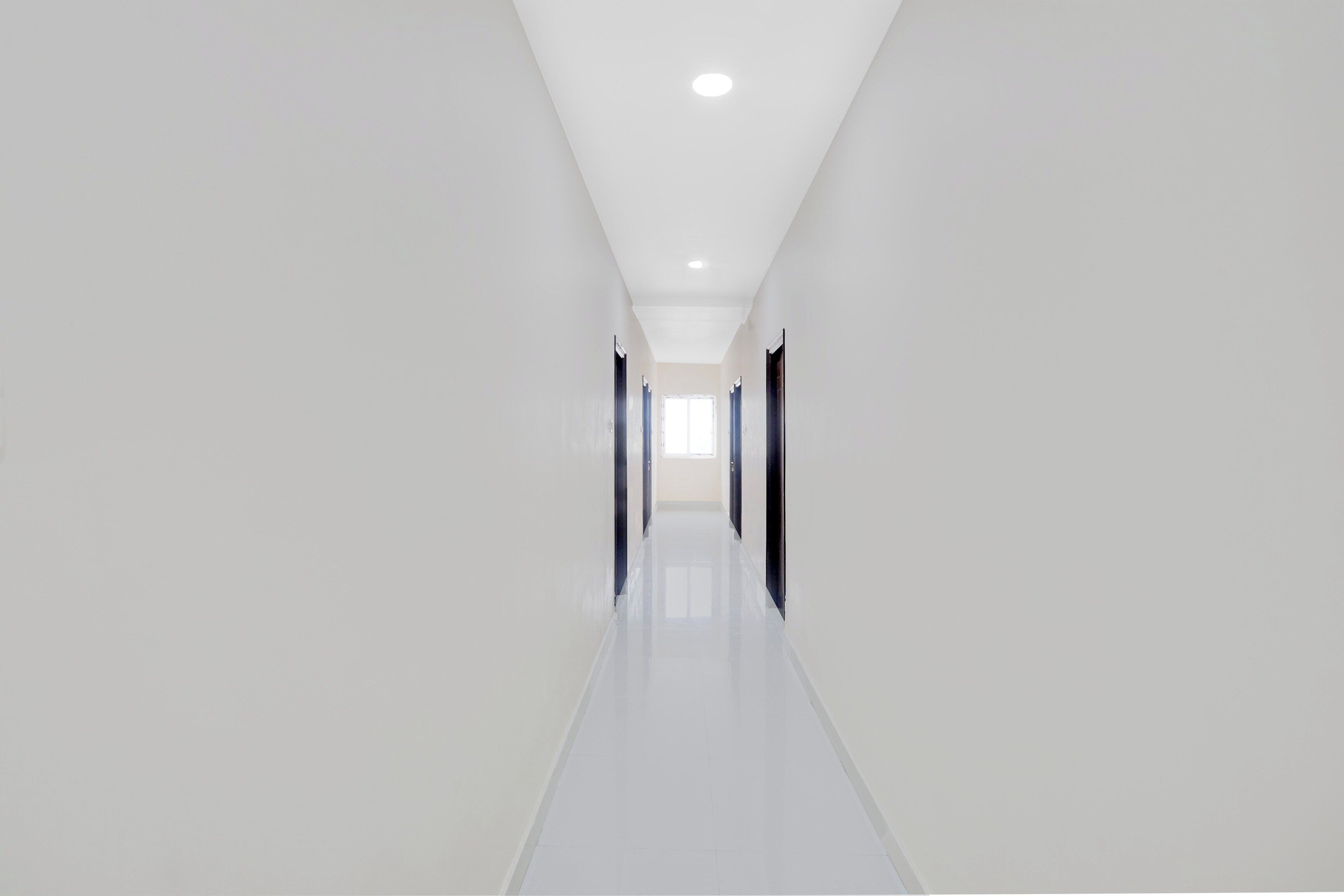 A long, narrow hallway with white walls and a glossy floor, leading to a door at the end.