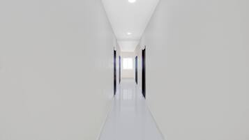 A long, narrow hallway with white walls and a glossy floor, leading to a door at the end.