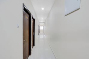 Un pasillo con una puerta de madera a la izquierda, un interruptor de luz y una placa con un número en la pared.