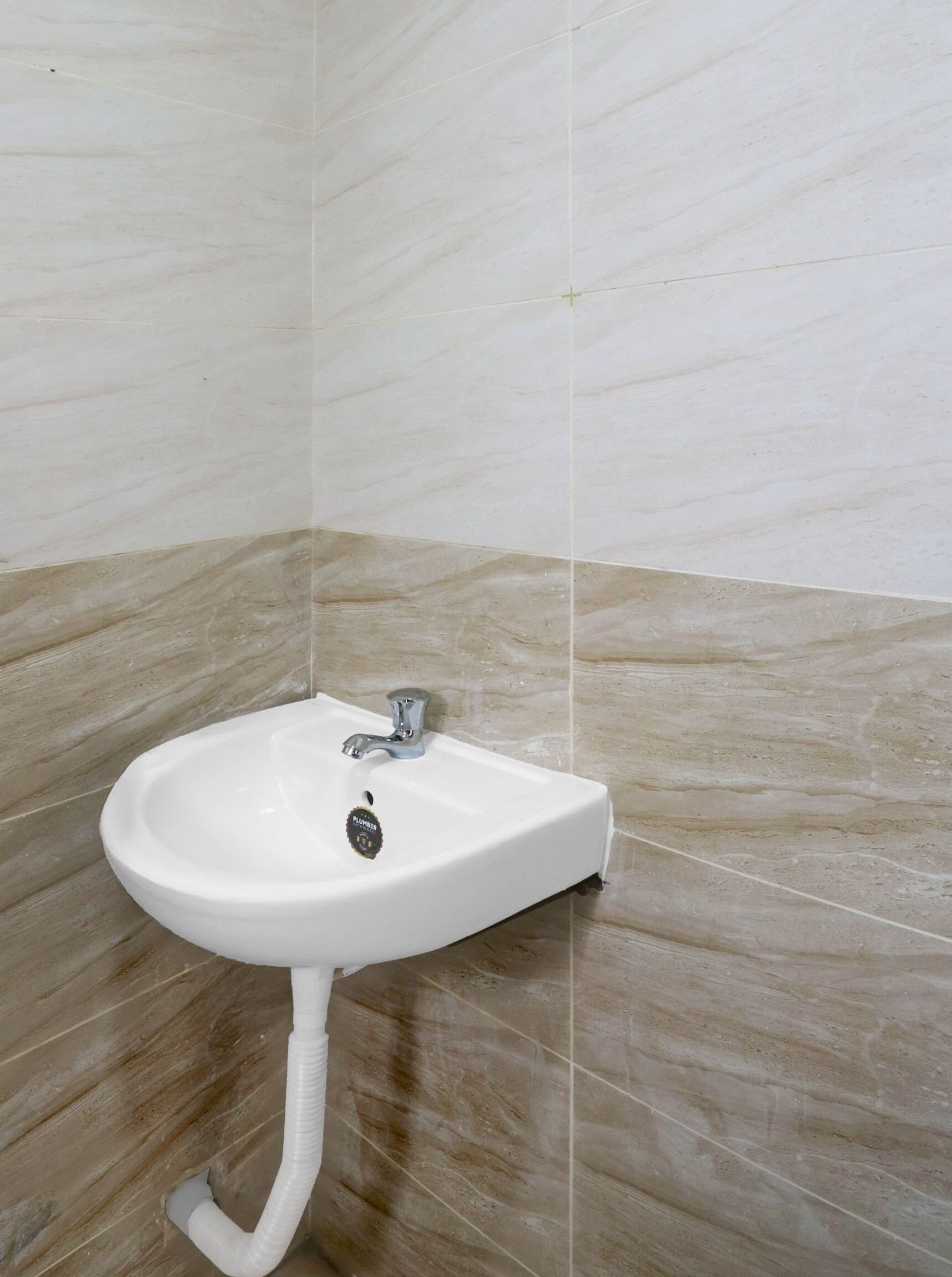 A white bathroom sink with a single faucet, mounted on a wall with beige and white tiles.