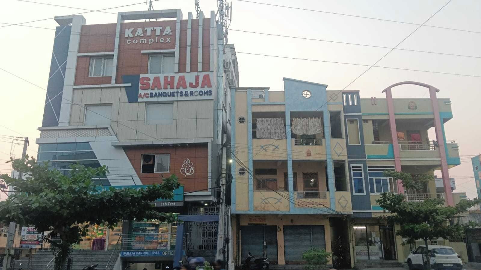 Un edificio de varios pisos con señalización que indica 'KATTA complex' y 'SAHAJA A/C BANQUETS & ROOMS'.
