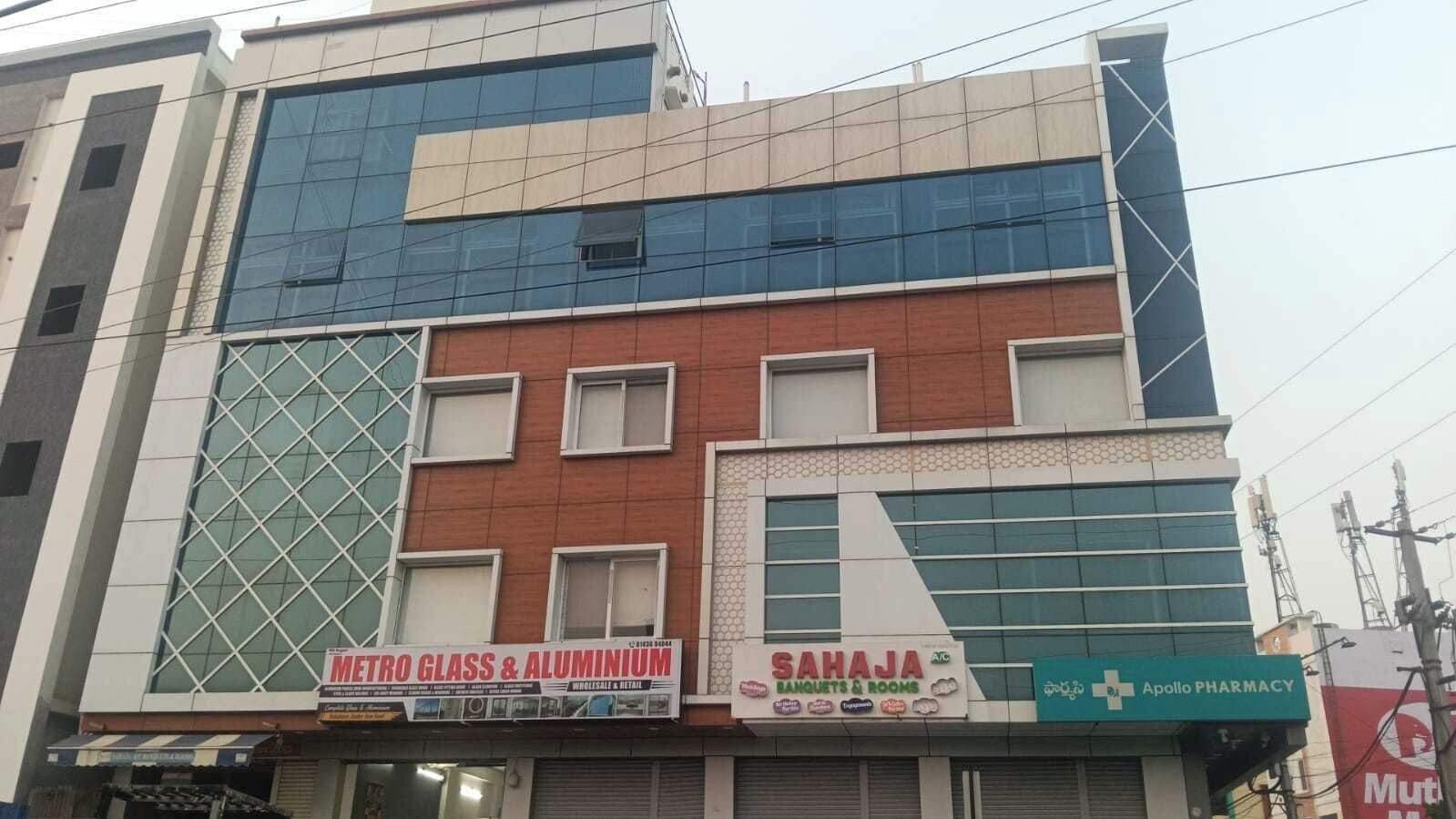 A multi-story building with commercial establishments on the ground floor, including a glass and aluminum store, a banquet and room service provider, and a pharmacy.