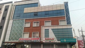 Un edificio de varios pisos con locales comerciales en la planta baja, incluyendo una tienda de vidrio y aluminio, un proveedor de banquetes y servicio a cuartos, y una farmacia.
