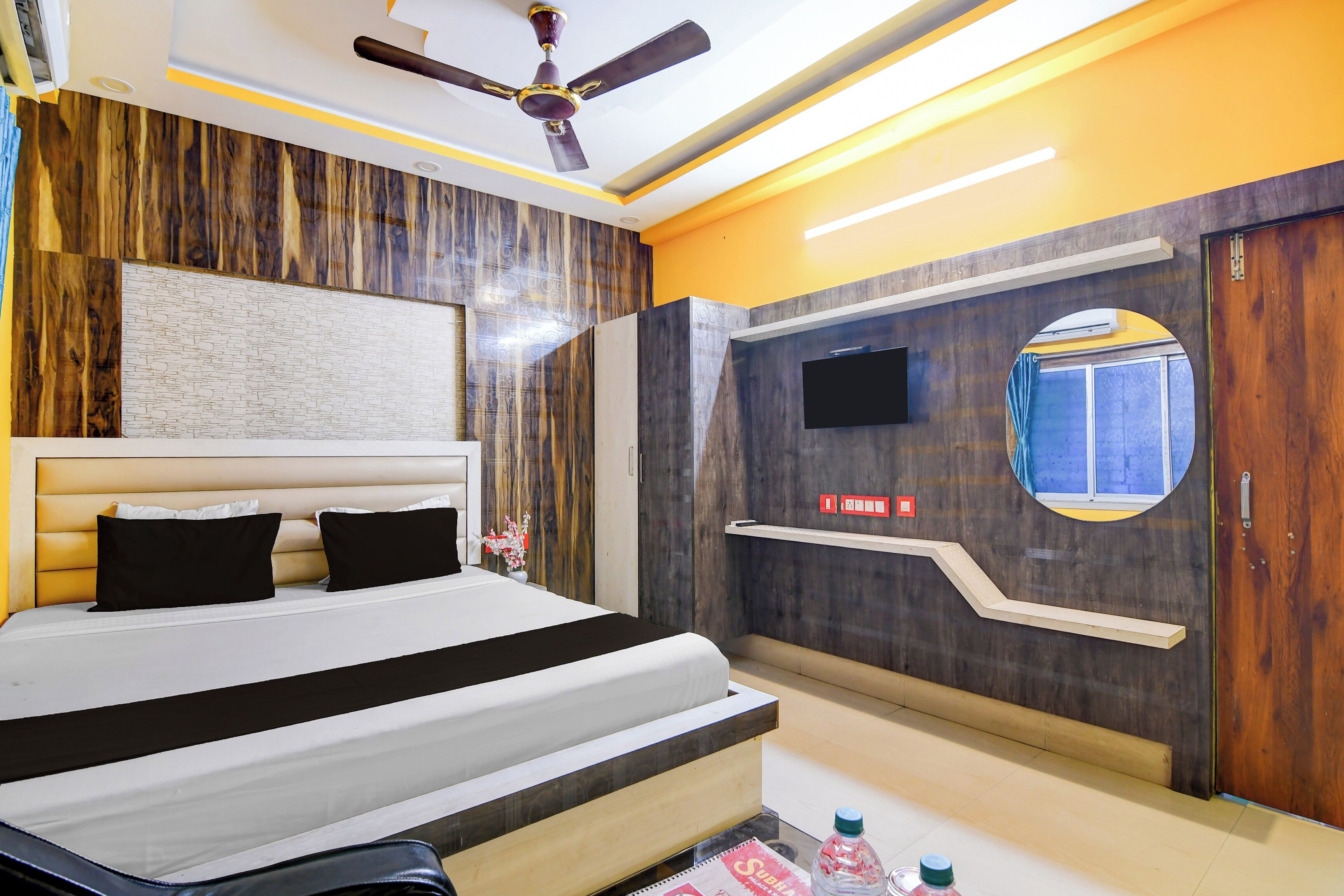 Un dormitorio moderno con una cama grande, ventilador de techo, televisor montado y una pared decorativa de madera.