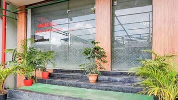 Entrada de un edificio con fachada de vidrio, escalones que conducen a la entrada y plantas en macetas.