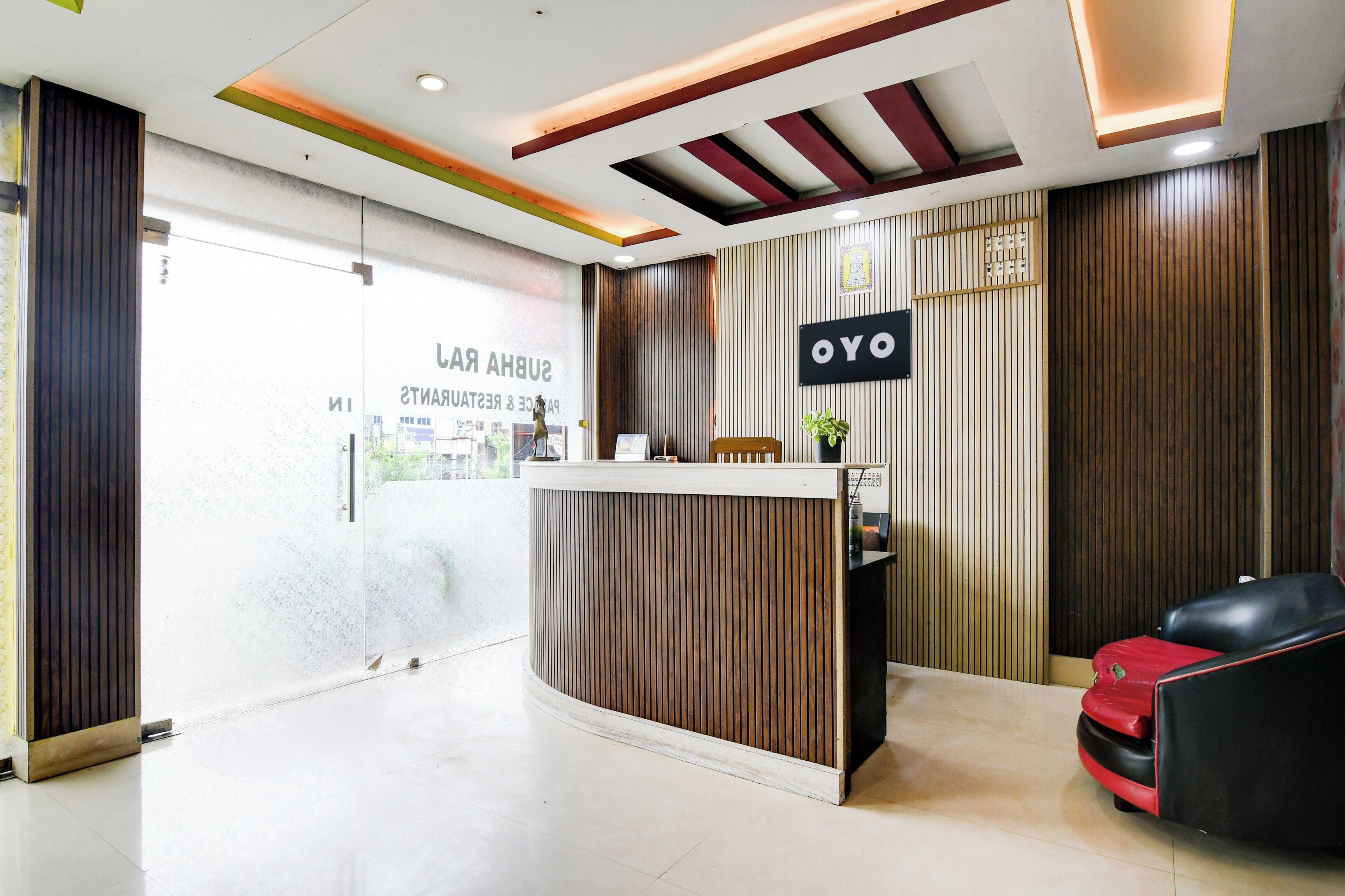 A reception area with a wooden reception desk, a black sign with 'OYO' on it, and a red and black seating area.