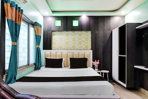 Una habitación de hotel con cama, cortinas, cabecero, una mesita y un armario.