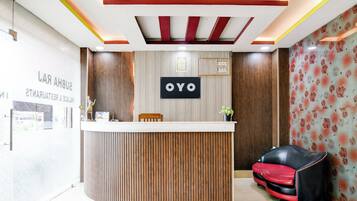 A reception desk with a sign that reads 'OYO' in a modern interior with wooden paneling and a red and black sofa.