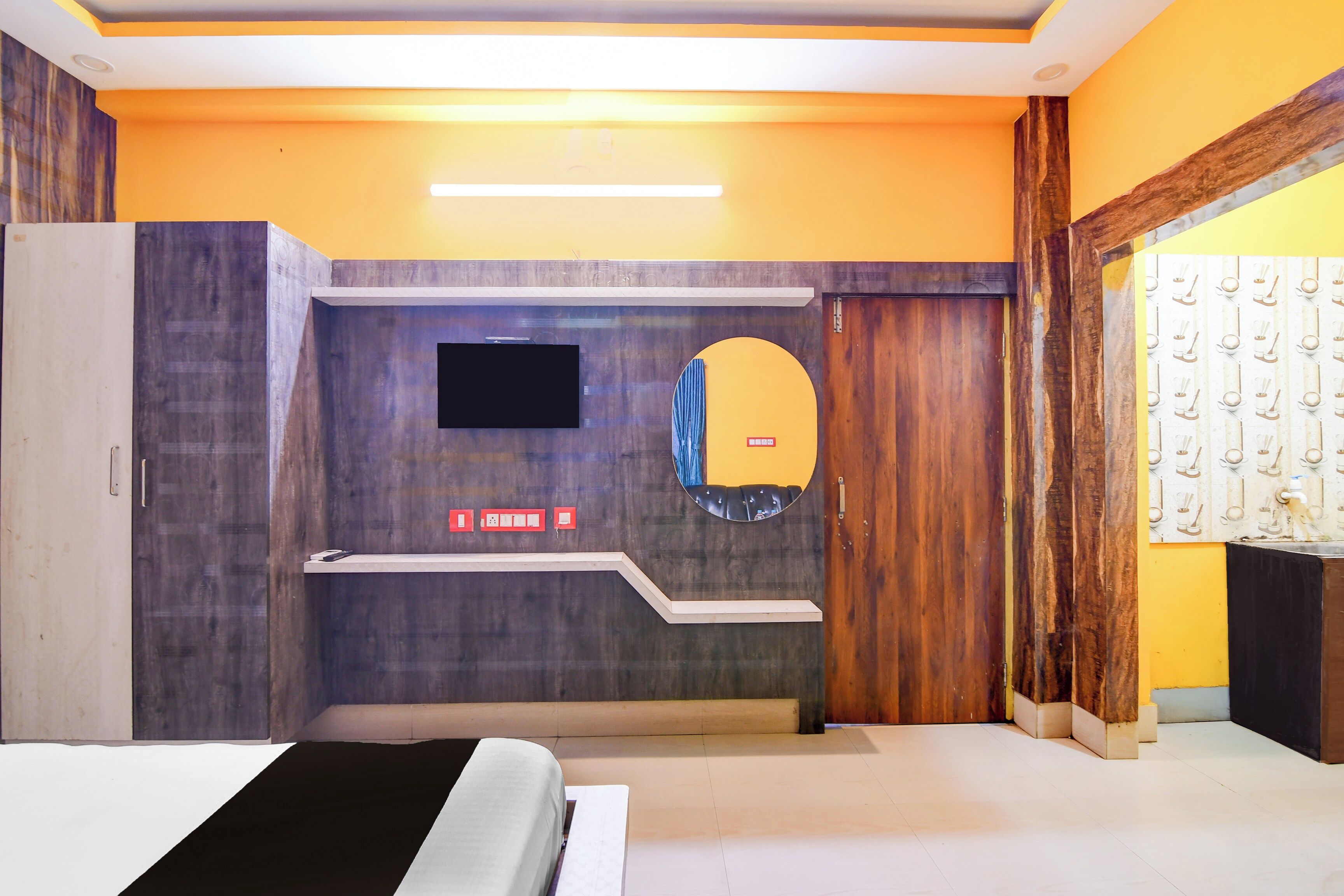 A hotel room with a bed, a flat-screen TV mounted on the wall, a mirror, and a wooden door.