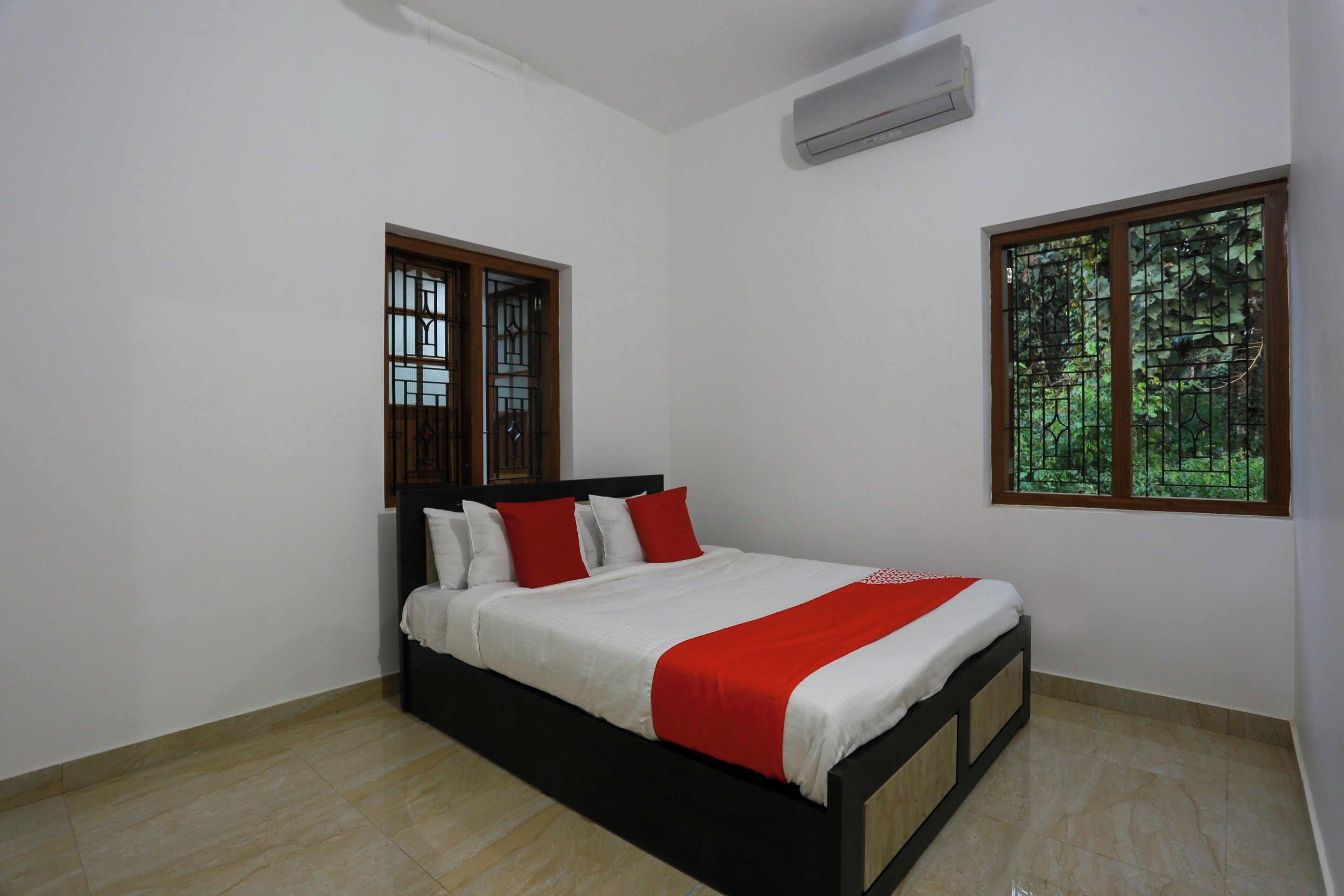 A bedroom with a bed, two windows, and an air conditioning unit.