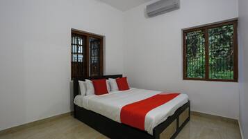 A bedroom with a bed, two windows, and an air conditioning unit.