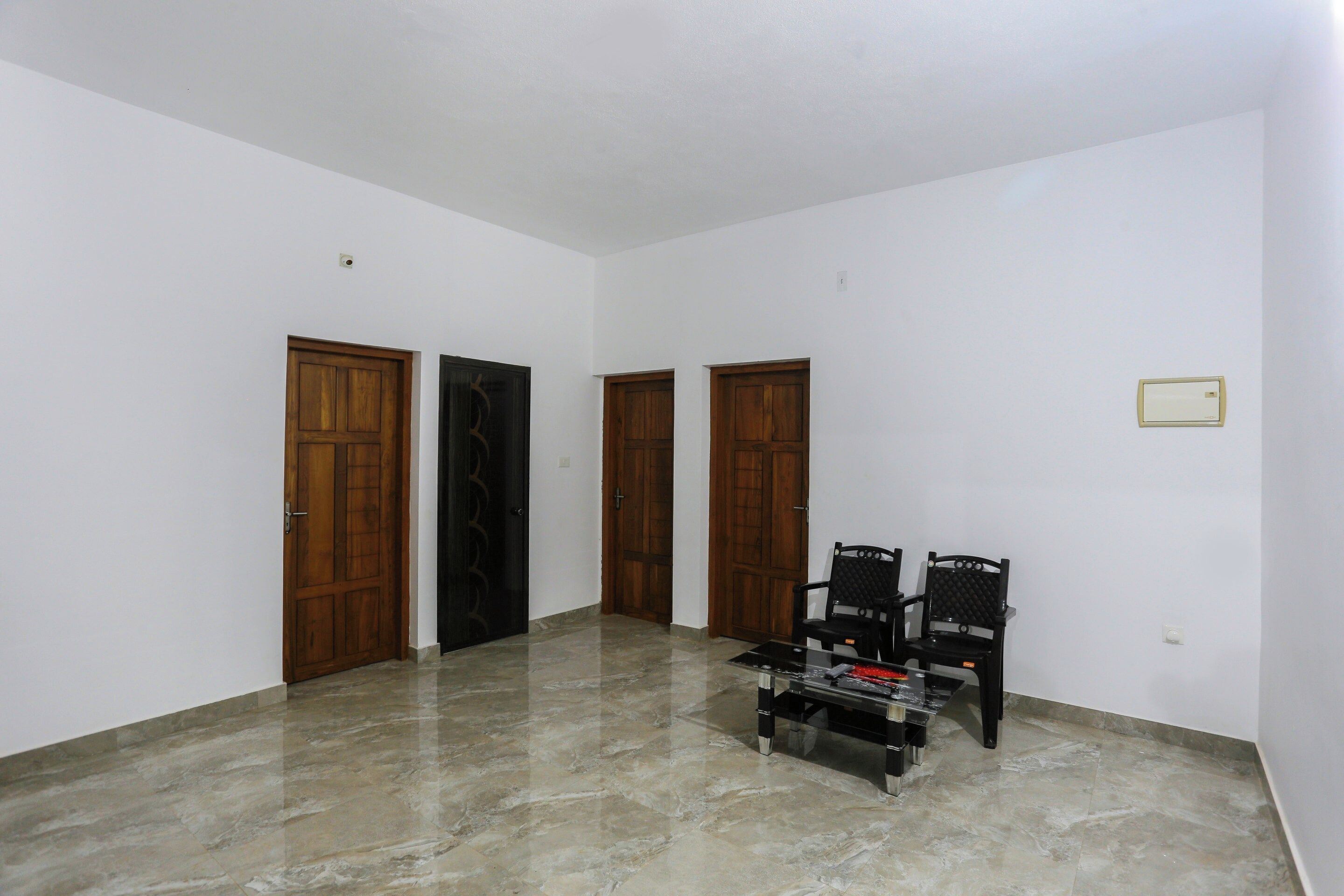 A room with a marble floor, two wooden doors, and two black chairs.