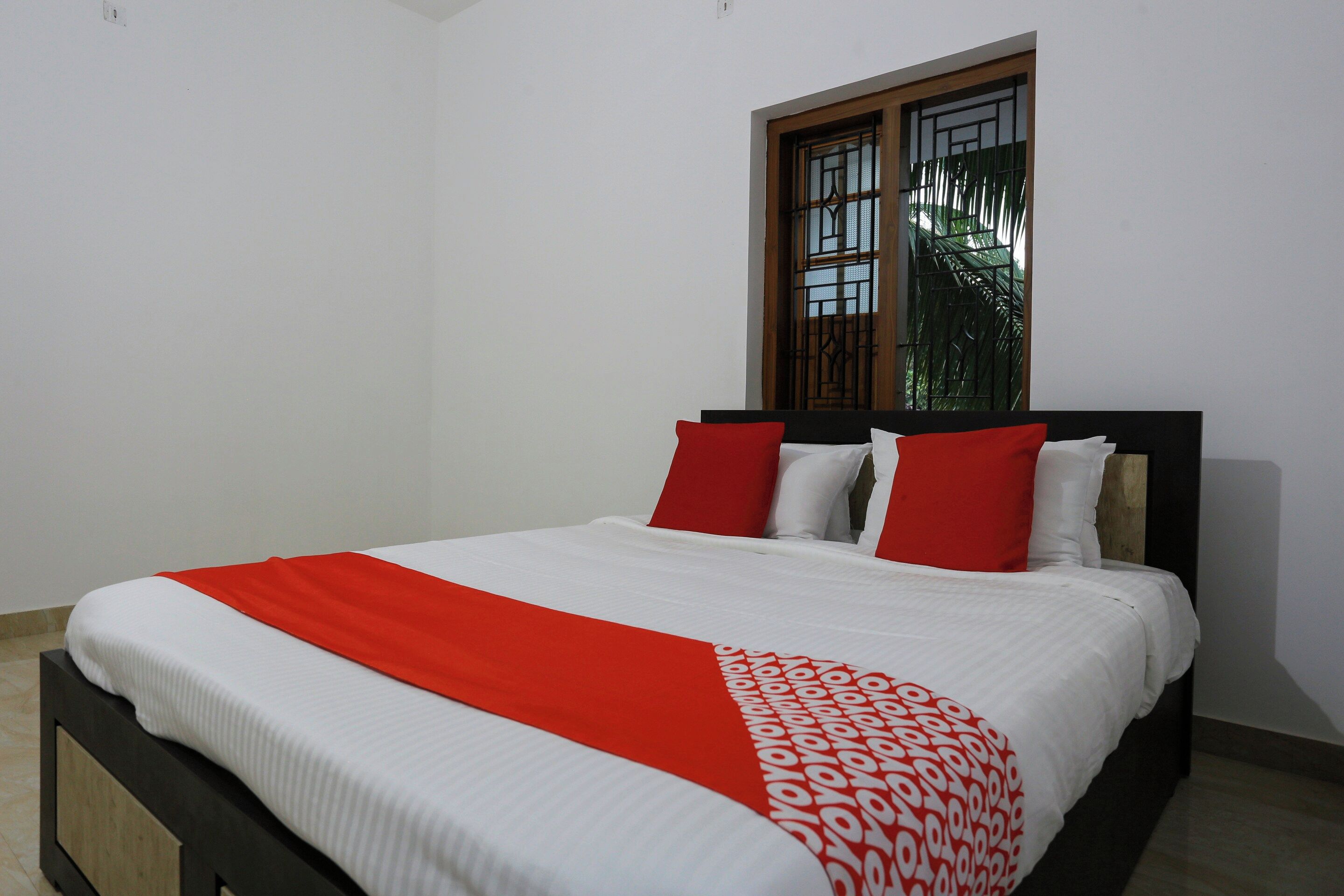 A bed with a white and red bedspread, a wooden headboard, and a window with metal bars.