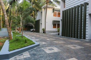 Un edificio moderno con un patio empedrado, rodeado de palmeras y un muro de piedra.