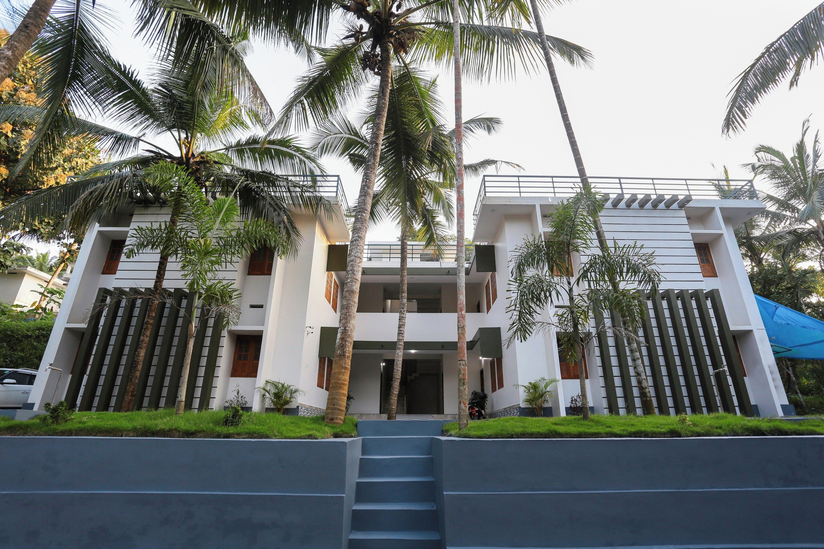 A modern two-story building with a central entrance, surrounded by palm trees and a blue awning.
