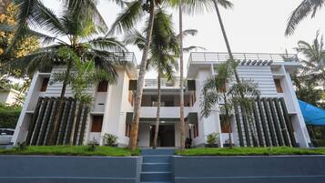 A modern two-story building with a central entrance, surrounded by palm trees and a blue awning.
