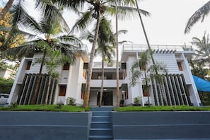 A modern two-story building with a central entrance, surrounded by palm trees and a blue awning.