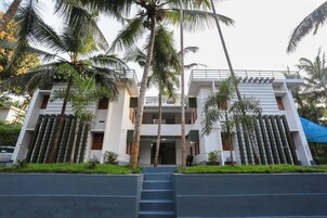 Un edificio moderno de dos plantas con una entrada central, rodeado de palmeras y un toldo azul.