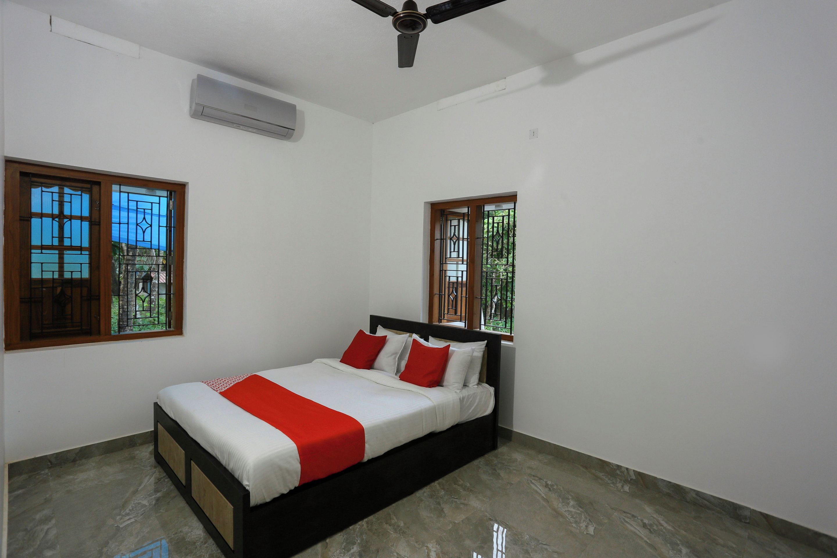 A bedroom with a bed, two windows with metal bars, an air conditioning unit, and a ceiling fan.