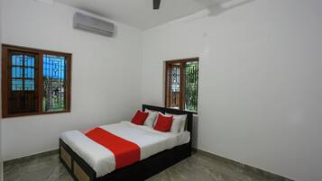 A bedroom with a bed, two windows with metal bars, an air conditioning unit, and a ceiling fan.