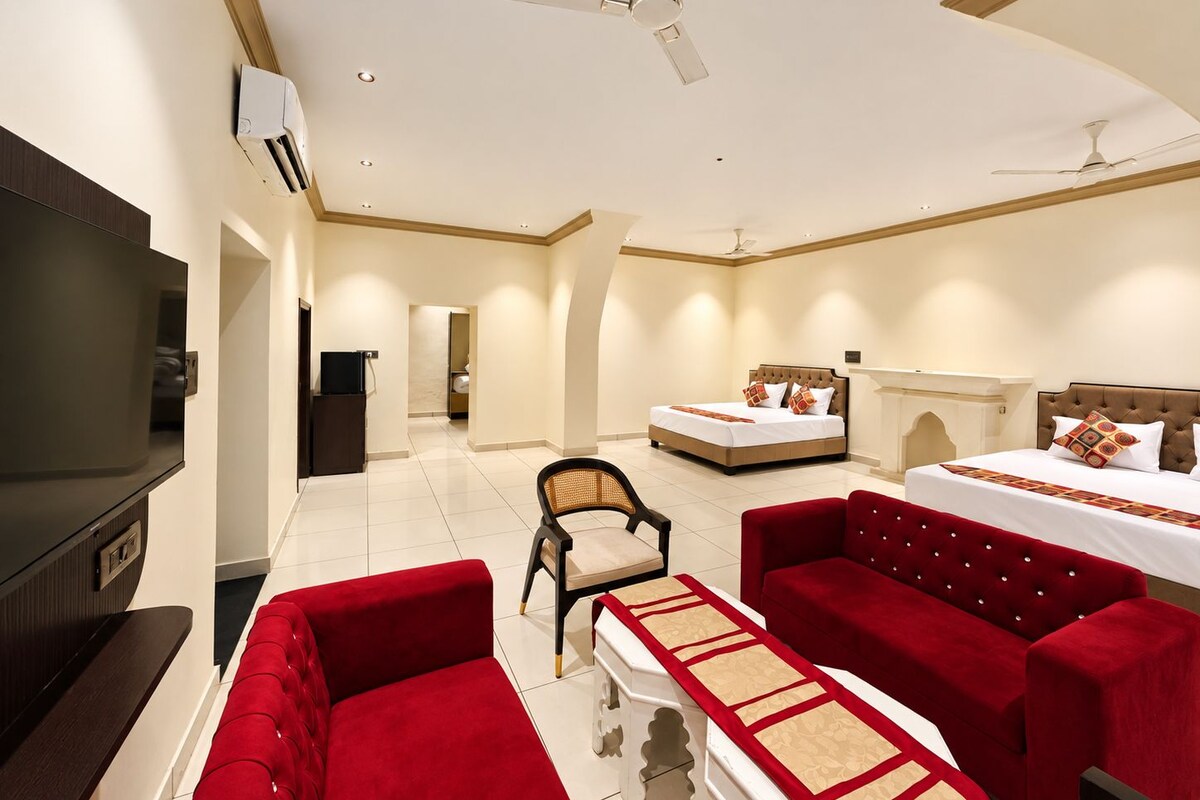 Une chambre d’hôtel équipée d’une télévision, de deux lits, d’un canapé rouge, d’une chaise et d’un ventilateur de plafond.