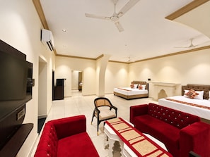 Une chambre d’hôtel équipée d’une télévision, de deux lits, d’un canapé rouge, d’une chaise et d’un ventilateur de plafond.
