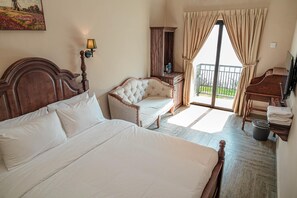 A hotel room with a large bed, a chaise lounge, a wooden desk, and a balcony with curtains. - The Farmhouse (Ipoh)