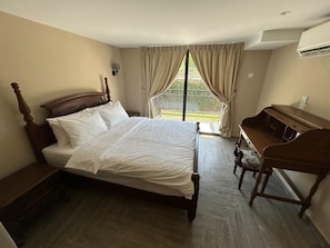 A bedroom with a wooden bed, a desk, and a view of the outdoors through a window with curtains. - The Farmhouse (Ipoh)