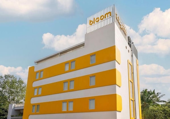 A multi-story building with a yellow and white facade, a prominent 'bloom' sign on the top, and a clear sky in the background. - Bloom Hotel - Jayanagar (Bengaluru)