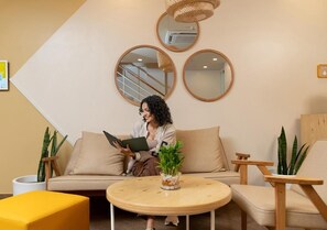 A person sitting on a sofa with a tablet, surrounded by plants and furniture in a room with a modern design. - Bloom Hotel - Jayanagar (Bengaluru)