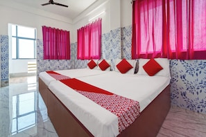 A hotel room with a large bed, red and white bedding, pink curtains, and a ceiling fan. - Hotel O Sri Sakthi Residency (Kanyakumari)