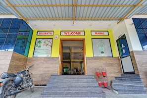 Fachada amarilla de un edificio con un reloj y carteles que dicen 'SRI SAKTHI', 'BIENVENIDOS' y 'MAHAL'.