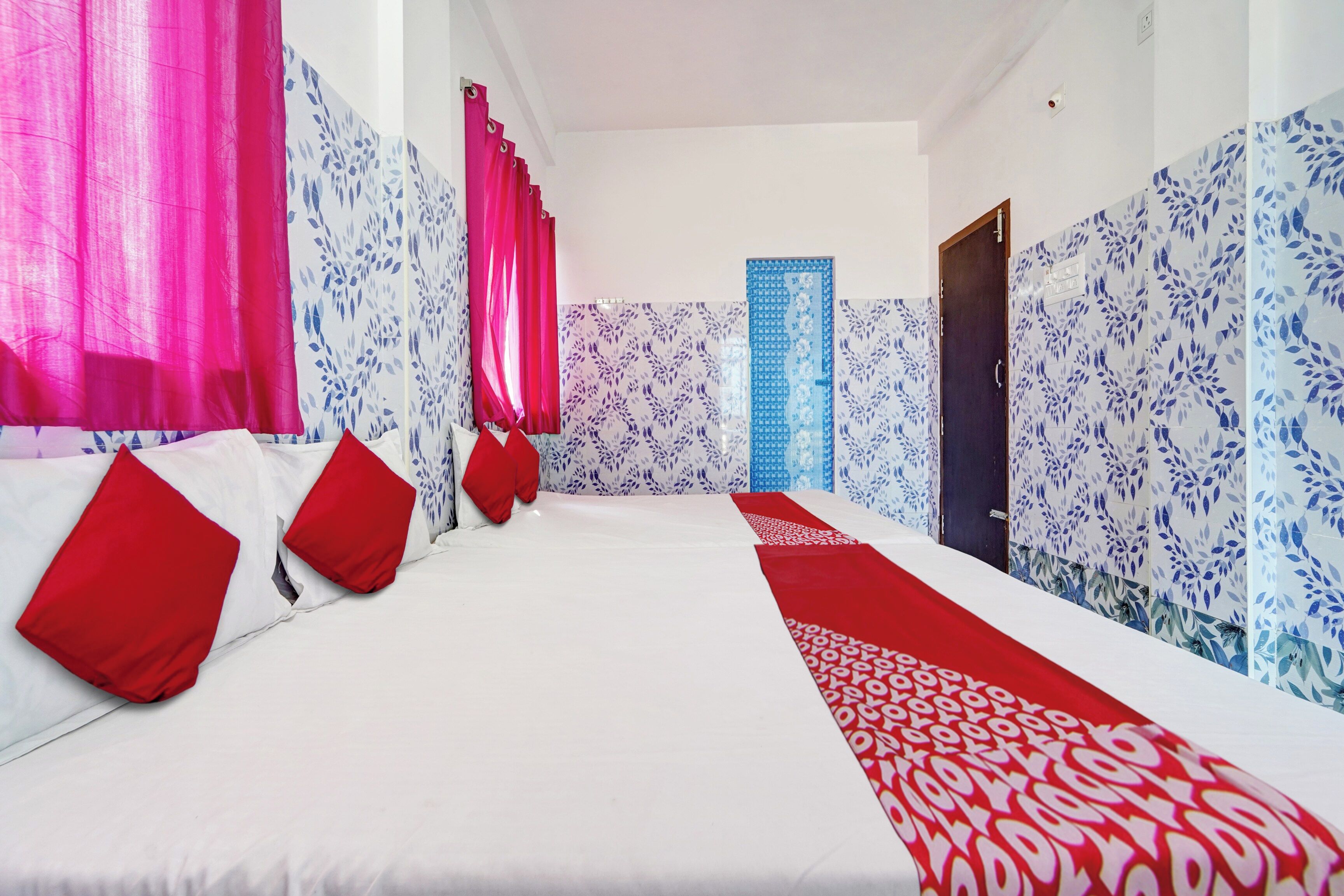 A hotel room with a large bed, red pillows, and patterned wallpaper.