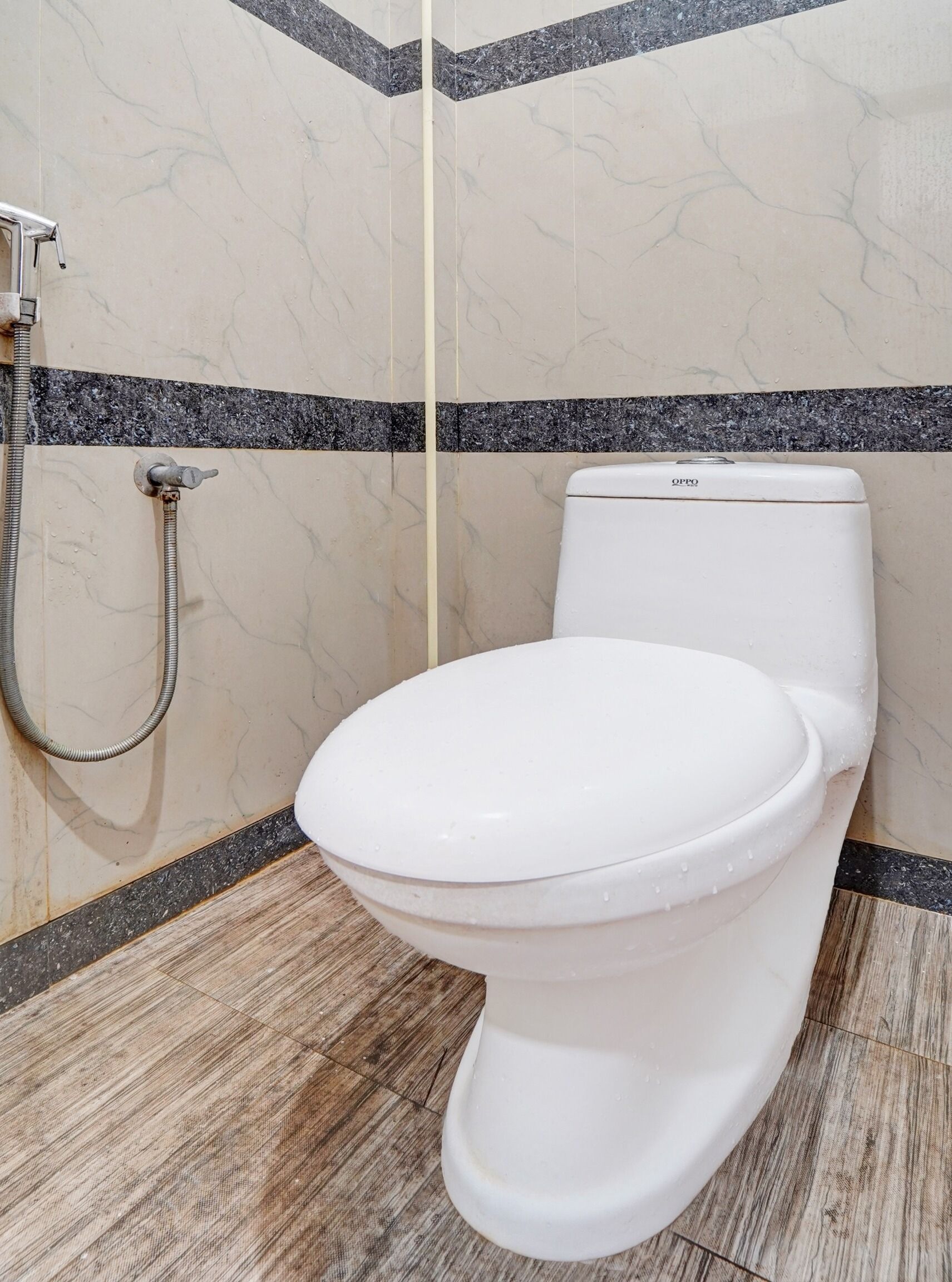 A white toilet with a control panel, a shower head, and a tiled floor with a marble pattern.