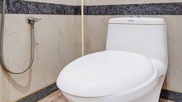 A white toilet with a control panel, a shower head, and a tiled floor with a marble pattern.