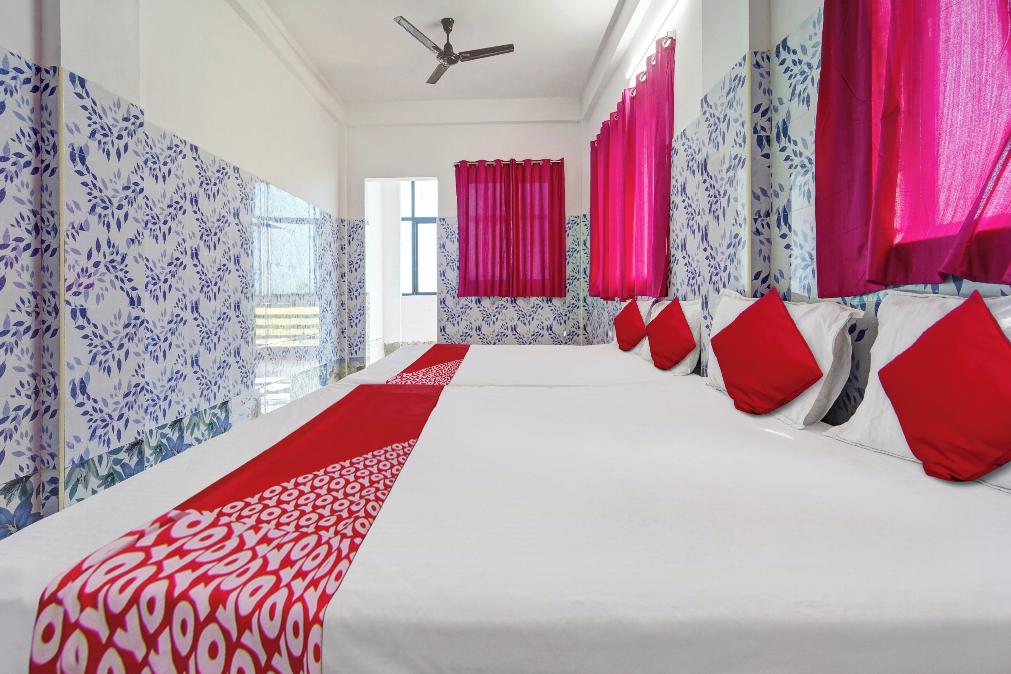 A hotel room with a large bed, red and white patterned runner, and red curtains.