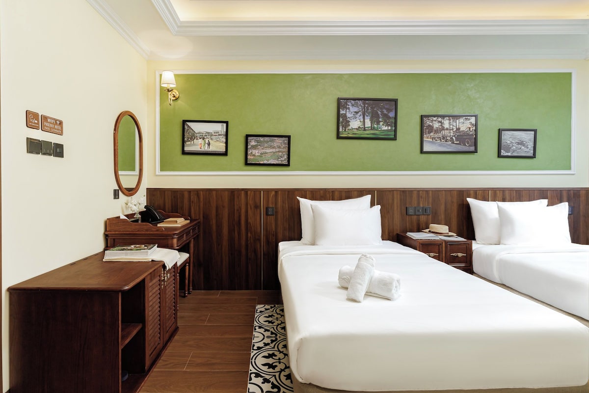 Ein Hotelzimmer mit zwei Betten, einem Schreibtisch mit Telefon, einem Spiegel und gerahmten Bildern an der Wand.
