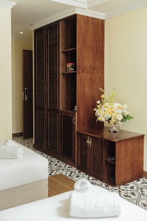 Ein Hotelzimmer mit Holzschrank, kleinem Schreibtisch, Blumenvase und zwei Betten.