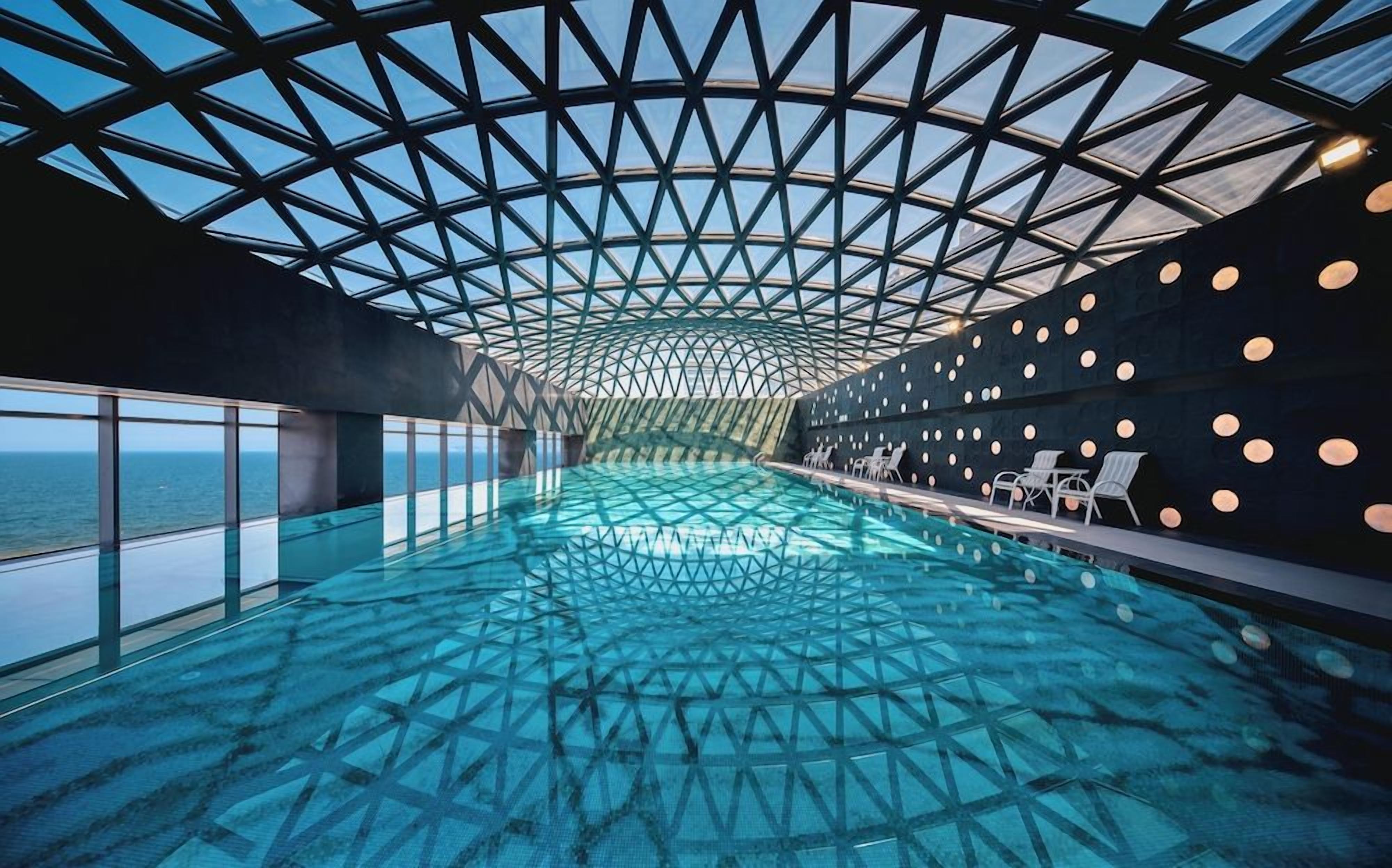 A modern infinity pool with a geometric ceiling design, surrounded by walls with circular light fixtures.