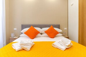 A hotel room with a bed, two pillows, a nightstand, a lamp, and towels. - New Listing (ROMA)