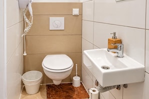A bathroom with a toilet, sink, and a trash bin. - Curtain Call Vienna 1BR near Stadthalle (Vienna)