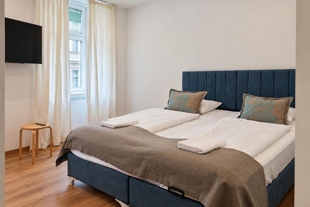 A double bed with a blue headboard, two pillows, and a blanket.