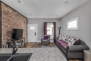 Un espace de vie compact avec un mur en briques, un téléviseur, un canapé et une fenêtre avec des rideaux.