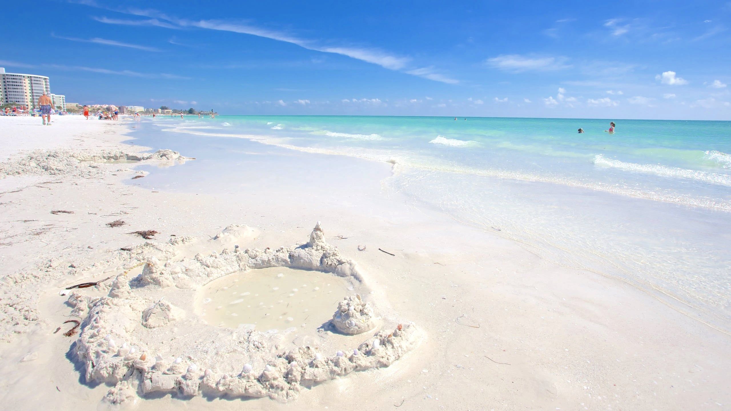 A beach with white sand, clear turquoise water, and a sandcastle.