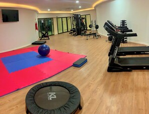 Ein Fitnessraum mit Trainingsgeräten, einer roten und blauen Matte sowie einem Trampolin.